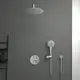 Duschanlage an einer grauen Wand, bestehend aus einem großen, runden Kopfbrause und einem Handbrausekopf. Steuerelemente und Anschluss von Ideal Standard sind sichtbar.